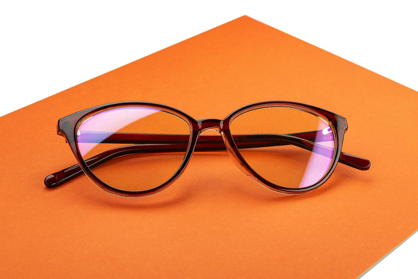 Stylish eyeglasses with a brown frame displayed on a vibrant orange surface in a minimalistic setup.